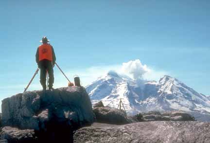 Photograph of geologist with instruments on tripods; mountain in background