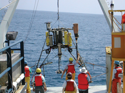 photograph showing scientists from the USGS lowering an array of scientific instruments into the water at Huntington Beach