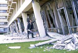photograph of a man standing next to the Olive View Hospital. Image shows the severe damage to the building as a result of the 1971 San Fernando earthquake in southern California
