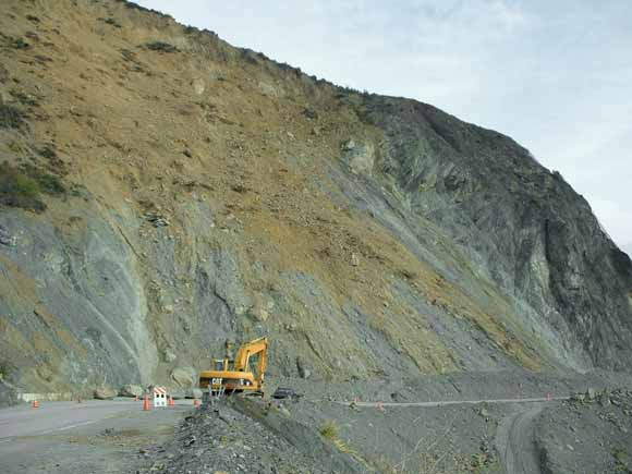 photograph of landslide being cleared from the road by an earth-moving machine
