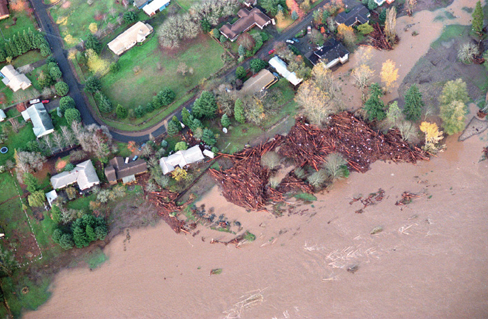 Photo of debris in backyards of houses next to flooding river. 