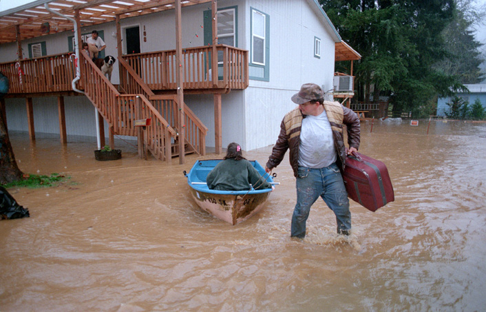 Photo of man knee-deep in flood water leaving his home.