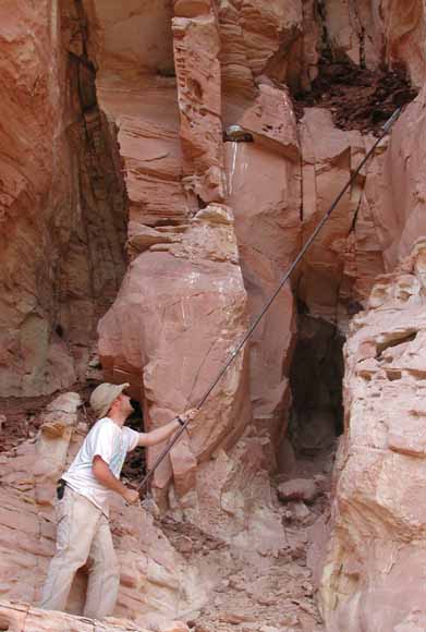 This is a photograph of a scientist probing a hole in a large cave. Figure caption will follow: 