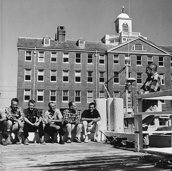 Dr. K.O. Emery holds an informal meeting with the WHOI-USGS project staff on the Institution's pier at Woods Hole.  These weekly lunch-time discussions offer a lively exchange of information amoung the scientists.  The ASTERIAS is docked in the background.  Personnel from left: Richard A. Tagg, USGS; Russel K. Paul, WHOI; John C. Hathaway, USGS; Dr. Richard A. Pratt, WHOI; Joseph A. Frothingham, Jr., WHOI; and Dr. Emery, WHOI.