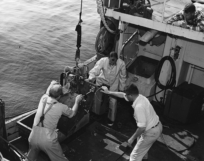 Geological Survey scientists aboard the Research Vessel GOSNOLD prepare a sampling bucket to go over the side. The bucket, on striking the sea floor, will close, taking a generous bite of sediment, shells, rock, etc. for laboratory analysis. From left: Dr. Robert H. Meade, John C. Hathaway, and Edward Bradley - all associated with the USGS - WHOI marine geology program.
