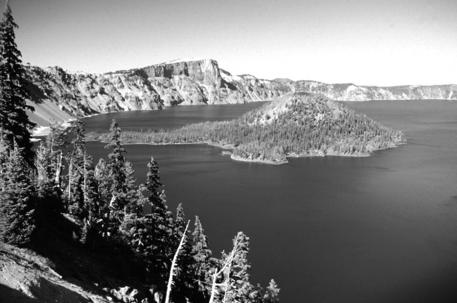[View of Crater Lake from the south rim of the caldera. The caldera formed 7,700 years ago by collapse of the volcano known as Mount Mazama during the largest explosive volcanic eruption in the past 400,000 years in the Cascades. The lava flows and volcanic deposits exposed in the caldera walls record the growth of Mount Mazama, which attained an elevation of roughly 12,000 feet before the caldera collapsed. The prominent cliff on the north rim of the caldera is Llao Rock, a lava flow that was erupted just 200 years before the caldera-forming eruption. The cinder cone and lava flows of Wizard Island were erupted within a few hundred years of formation of Crater Lake caldera.
<i>(USGS photograph taken by David Wieprecht, Cascades Volcano Observatory.] 