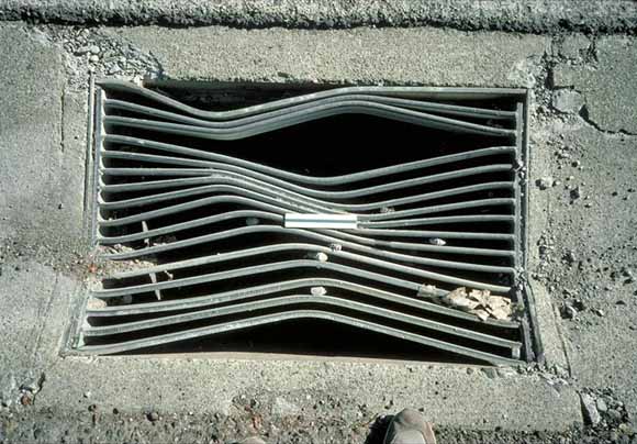 photo of storm-drain grate that has been bent along a diagonal by faulting
