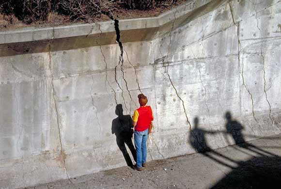 photo of geologist viewing a large crack in a concrete wall; the wall is twice as tall as the person.