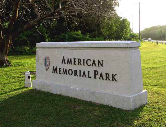 Photograph of stone entrance sign on a lawn showing Park Service logo and the name American Memorial Park