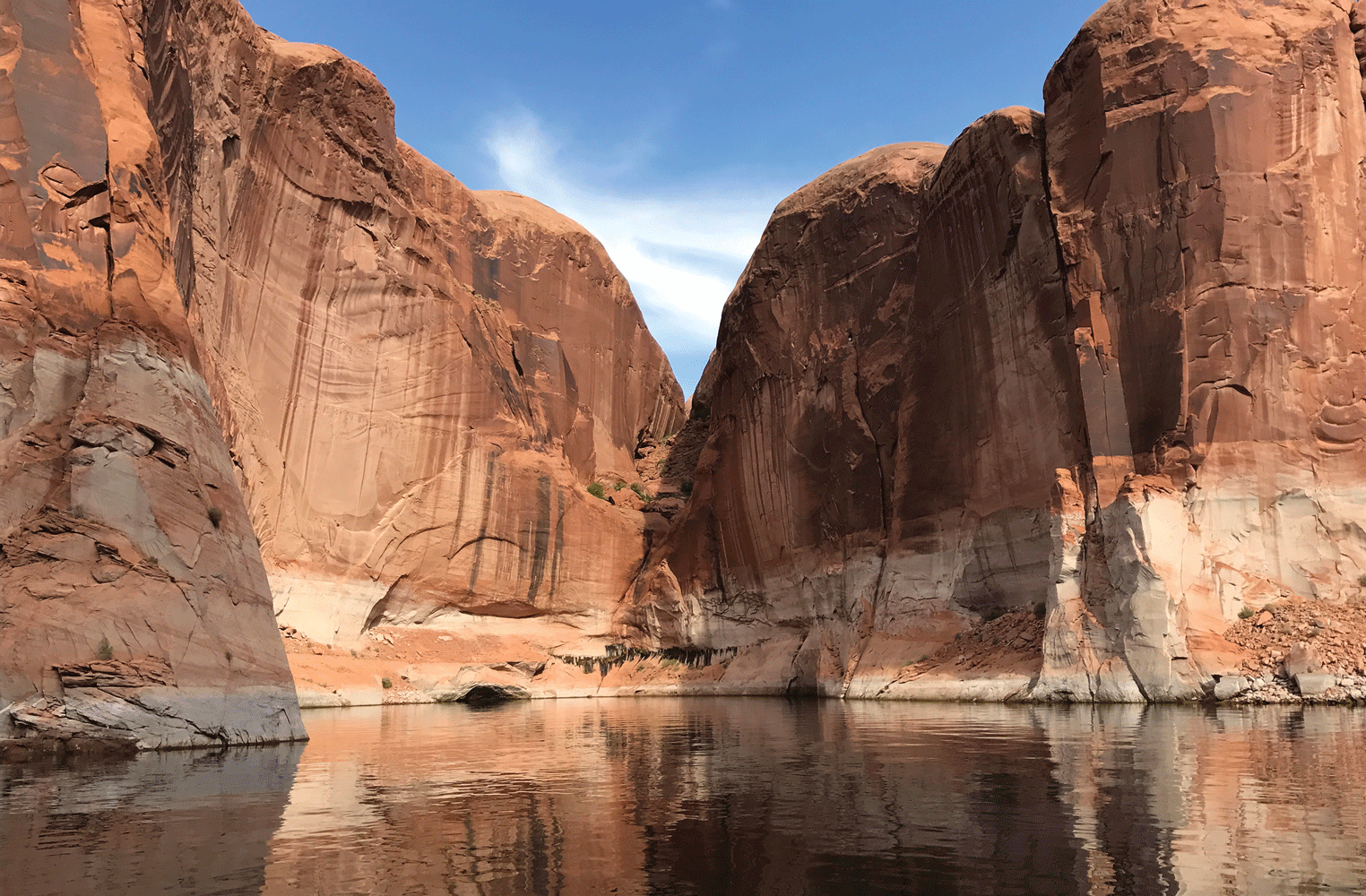 Under a blue sky, tall rocky cliffs enclose part of a lake.