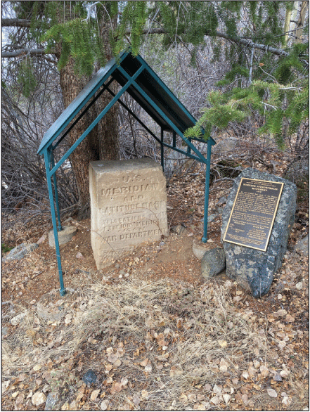 Rock monument, covered by a small, peaked, metal canopy, protruding from the ground.
A plaque is mounted on an adjacent rock.