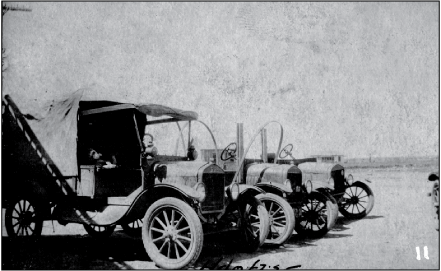 Three trucks sitting side-by-side outdoors on a plain dirt surface.