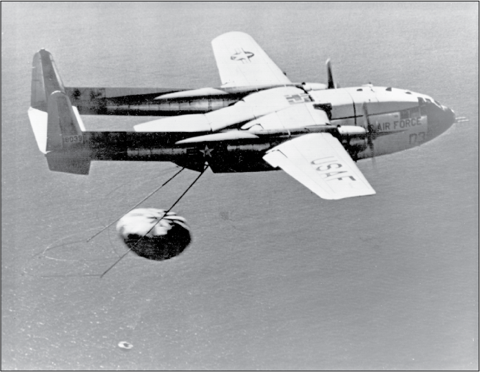 Airplane with a mechanical “hook” flying over water and preparing to hook the parachute
of a descending capsule below.