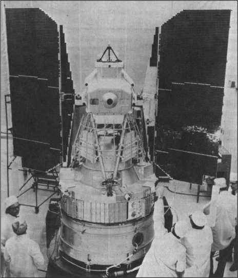 Five people dressed in lab coats stand around the base of the satellite.