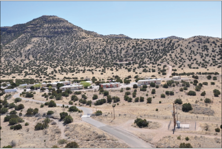 Figure 1 alt text. A series of buildings in the foreground and mountains in the background
in a landscape dotted with shrubs.