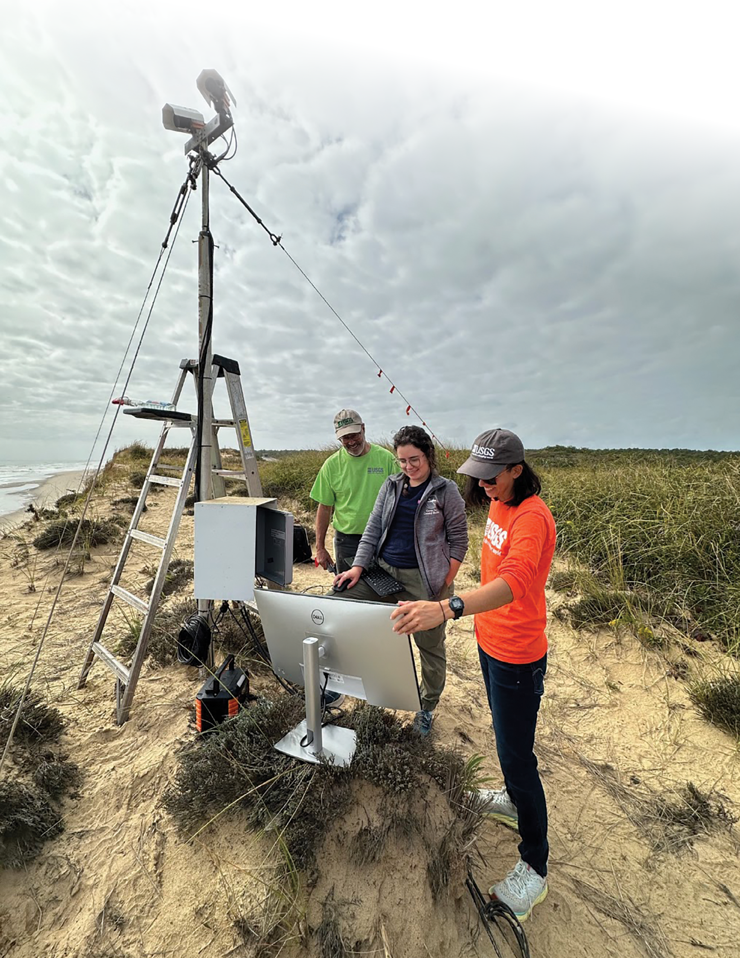 The researchers stand outdoors, near the CoastCam, and look at a computer monitor.
The CoastCam appears to extend up from the bluff about twice as high as a stepladder
beside it.