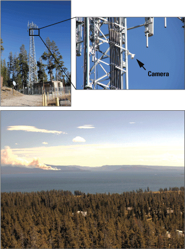 4. A tall tower with a camera mounted on it. A forested landscape in the foreground
and a smoke plume rising and hills in the background.