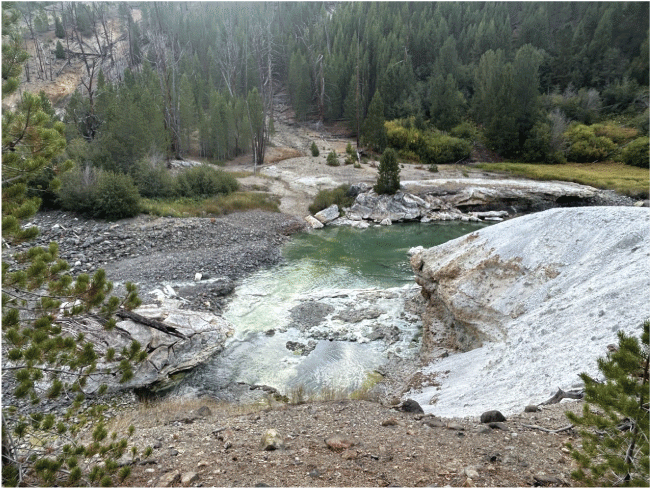 12. A pool of water surrounded by a rocky landscape and trees with a forested hill
in the background.