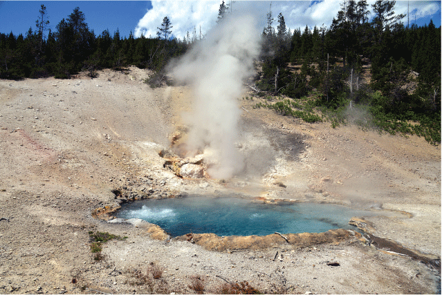 13. A blue pool of water and steam rising from it in a rocky foreground with a forest
hillside in the background under a blue sky.