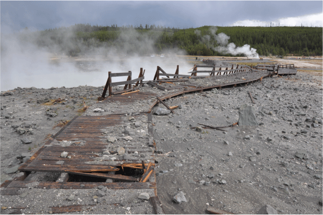 24. A damaged and broken boardwalk surrounded by debris from a thermal pool explosion.
Steaming thermal pools can be seen off to the left and in the background.