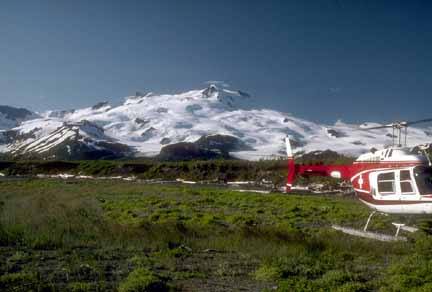 Photograph of volcano with helicopter in meadow in foreground