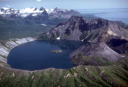 Photograph from air of volcano with lake in crater and green vegetation on flanks