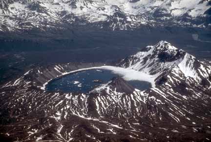 Photograph from air of volcano with dusting of snow and partially frozen lake in crater
