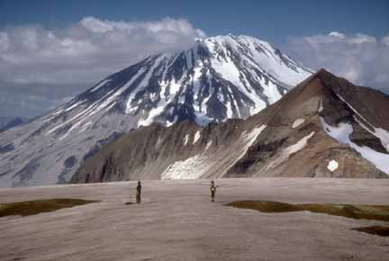 Photograph of volcano in background and two geologists in middle foreground