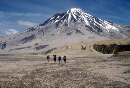 Photograph of volcano in background and four pack-carrying field workers in foreground