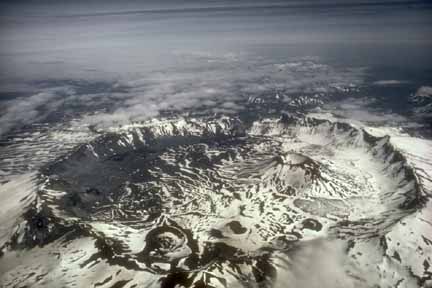Photograph from the air of snow-covered caldera with cones and craters and lake inside