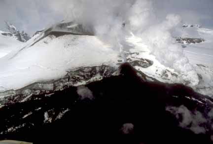 Photograph from air of dark, steaming lava flow at base of snow-covered cone