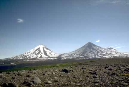 Photograph of two conical volcanic peaks, the left one with snow on its flanks, the right one dark with new ash