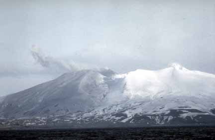 Photograph of ash and snow-covered slopes of volcano, steam cloud from crater