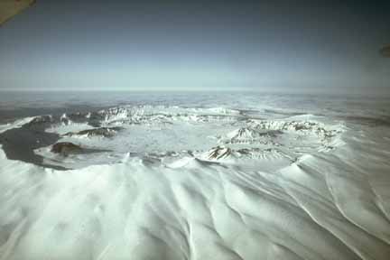 Photograph from air of snow-covered caldera containing darker cones and craters