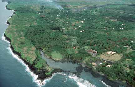 photo 060.  Low-elevation oblique aerial photo of lava flow nearing lagoon and ocean; houses between shore and lava