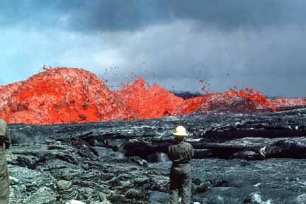 photo 090.  Photo of geologist in foreground watching billowing lava gushing from fissure in background