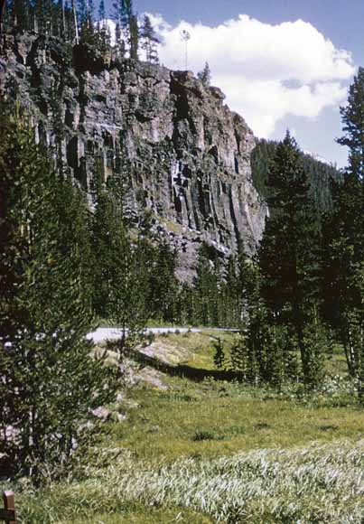 Photo of volcanic cliff with road beneath it and meadow in the foreground