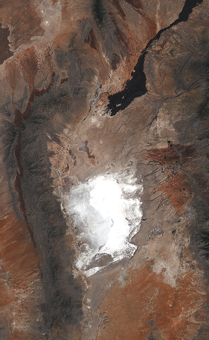 A patch of white sand can be seen in the center of the image, surrounded by dark red
                     and brown earth.