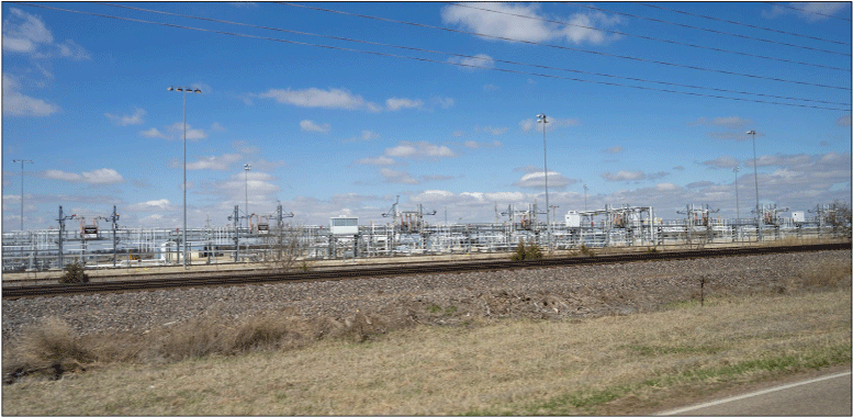 Photograph taken from a highway showing above ground gas storage infrastructure, including
                        piping, tanks, and a railroad.