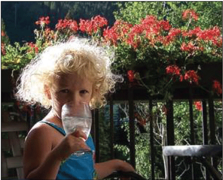 Girl drinking water from a glass while standing outside.