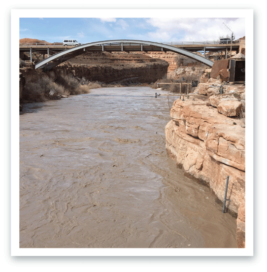 A river experiencing high flow with high turbidity passes a streamgage.
