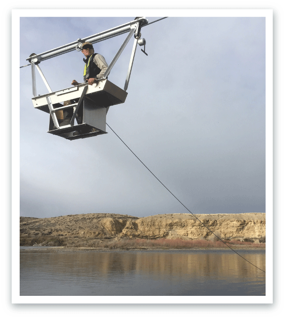 Person standing on a riverbank with measuring equipment floating in the water.
