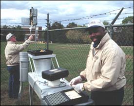 Photograph of USGS scientists inspecting an air deposition station used to monitor the content of harmful particles and pathogens in transoceanic dust