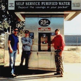 A color photograph of three men standing in front of a drinking water dispensing kiosk.