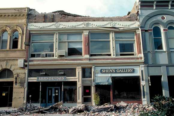 photo of damages store fronts with rubble on sidewalk out front