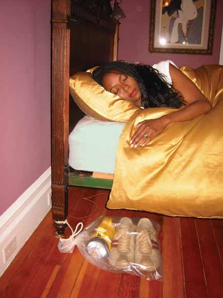 photo of woman asleep in bed with a clear-plastic, drawstring-closed bag tied to the bed leg on the floor.  The bag contains shoes and a flashlight