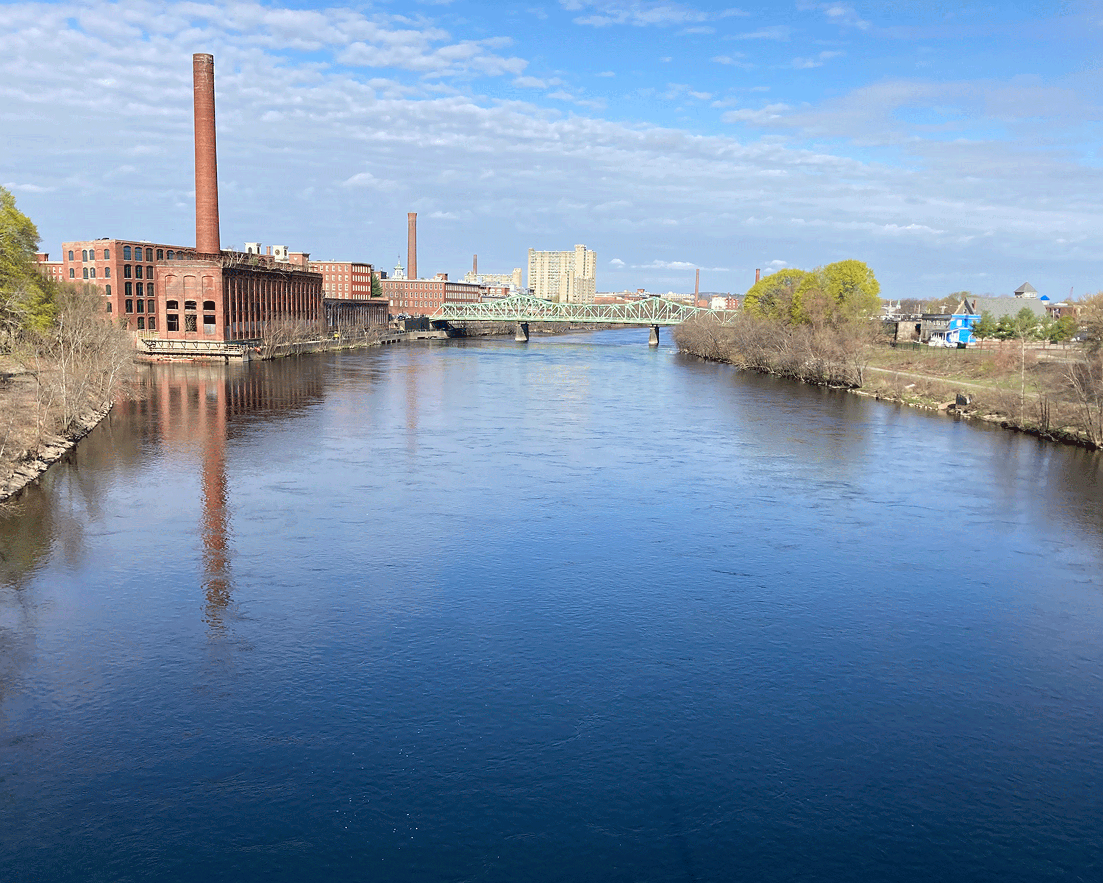 Photograph of the Merrimack River flowing through an urban area with historic brick
                     mill buildings and a truss bridge.