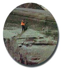 A color photograph of a person standing on the side of a mountain.  Photo: USGS, C. Gardner