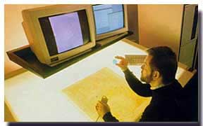A color photograph of a man sitting  a two-computer light table for digital mapping. - Photo: USGS