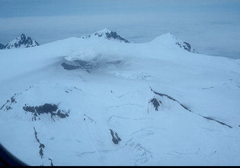 Figure 10. Aerial view of the summit area of Makushin Volcano. Steaming phreatic crater and snow darkened by ash visible in upper left center.